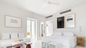 Ett modernt hotellrum med en vit säng, en soffa, ett soffbord och ett litet sidobord. På väggen hänger inramade citat och i taket sitter en takfläkt.