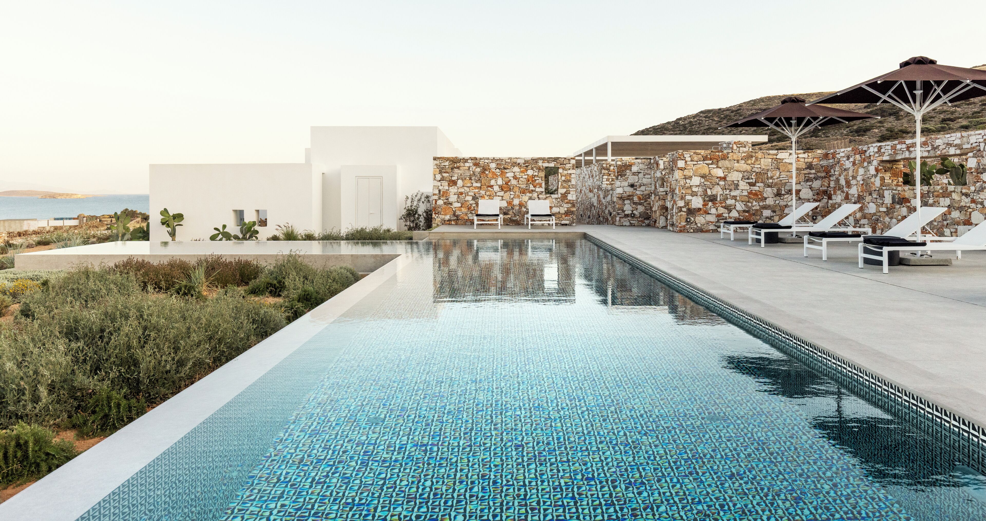 A swimming pool with a stone wall and lounge chairs.