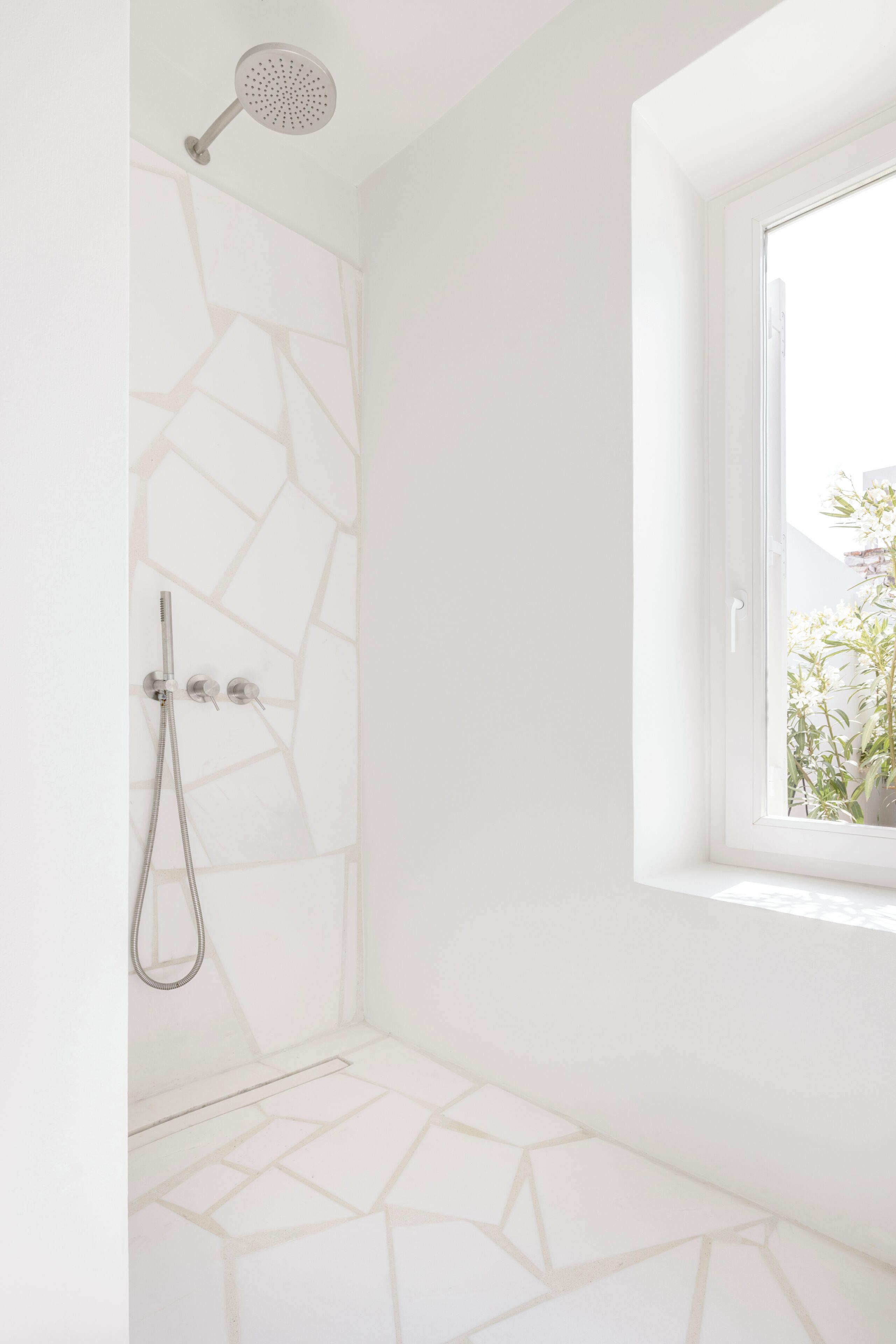Un baño con ducha, ventana con vistas y suelo de baldosas geométricas.