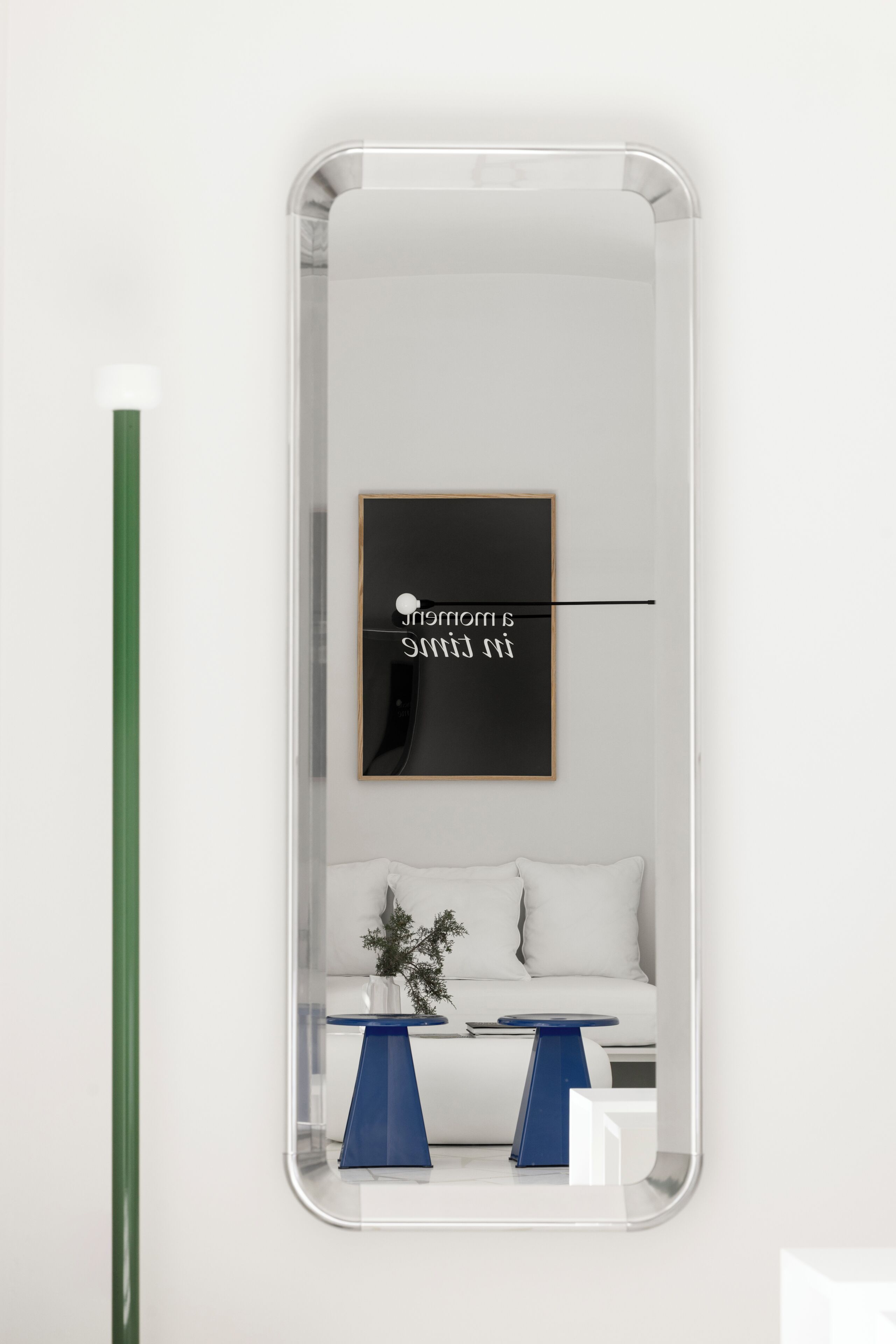 A modern room with a white sofa, a small table with a blue base, and a framed artwork on the wall.