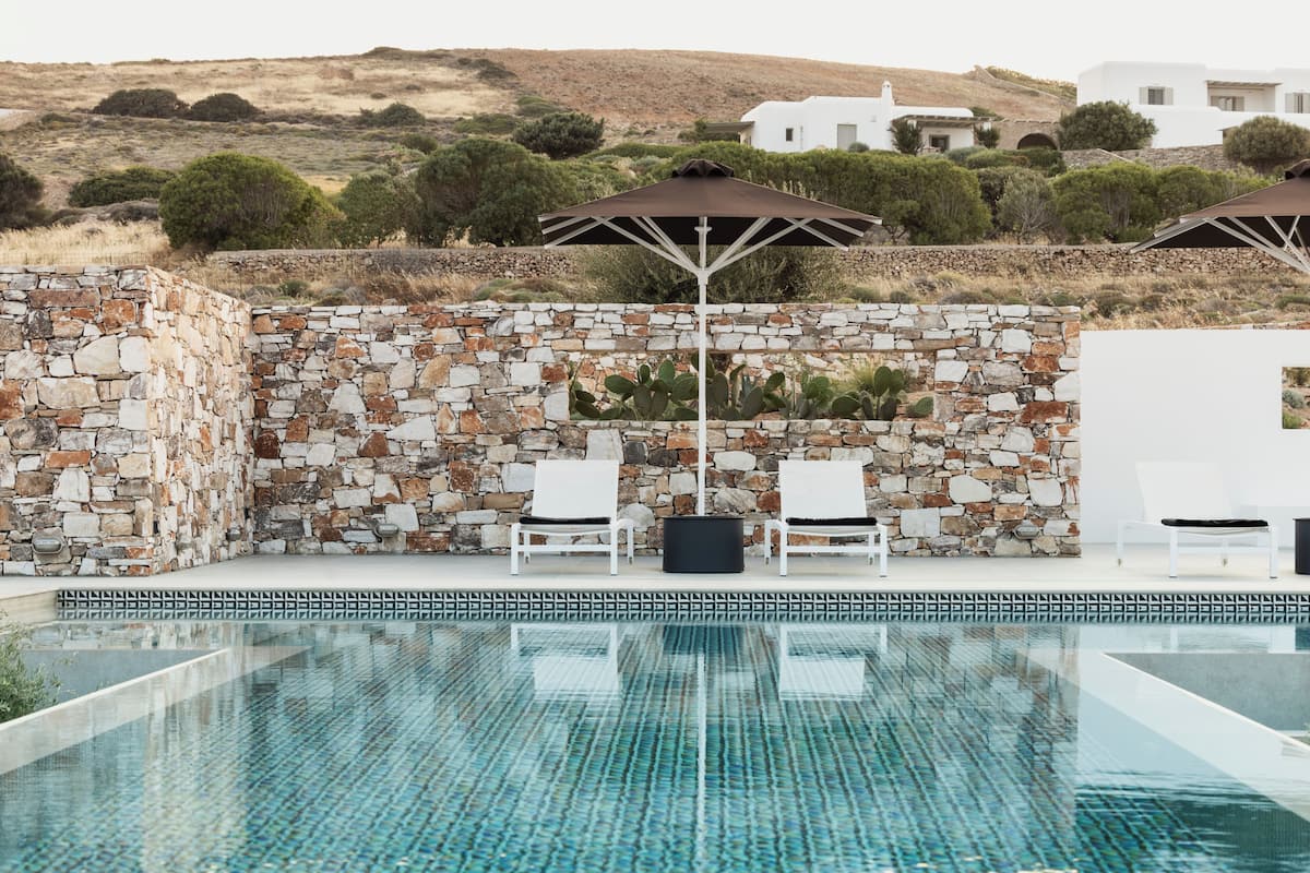 Una piscina con paredes de piedra y sillas de descanso blancas.