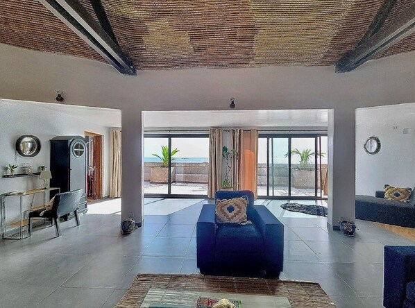 A spacious living room with a large sofa, a coffee table, and a view of the outdoors through large windows.