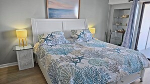 Ein Schlafzimmer mit Bett, Nachttischen, einem Bild und Meerblick durch ein Fenster.
