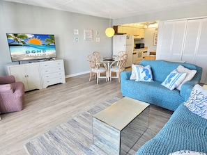 Ein Wohnzimmer mit Fernseher, Sofa, Sesseln und einer Küche im Hintergrund.