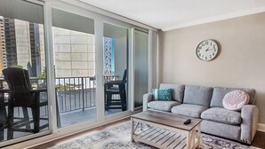 A living room with a grey sofa, a patterned rug, a wooden coffee table, and a wall clock. - Oceanfront 3rd Floor Condo with Pool just steps from the Atlantic Ocean! Quay #301 (Ocean City)