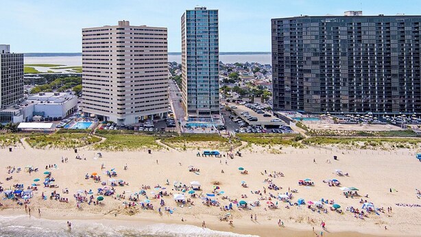 A beach with numerous umbrellas and people, surrounded by high-rise buildings. - Oceanfront 3rd Floor Condo with Pool just steps from the Atlantic Ocean! Quay #301 (Ocean City)