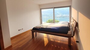 Camera da letto con pavimento in legno, un letto, un'ampia finestra e vista sulla città.
