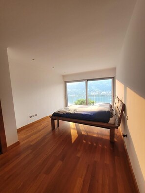 A bedroom with a wooden floor, a bed, a large window, and a view of a cityscape. - The Vision of Luxury Switzerland (Collina d'Oro)