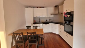 Una cucina compatta con mobili bianchi, un tavolo da pranzo in legno e un forno integrato.
