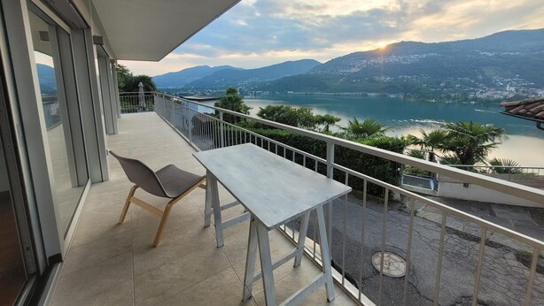 Un balcone con tavolo e sedie, vista su un lago e montagne.