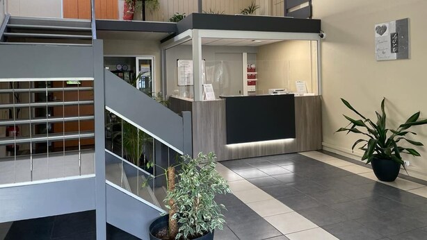 A modern hotel lobby with a reception desk, a staircase, and potted plants. - BE MYHOTEL (Évreux)