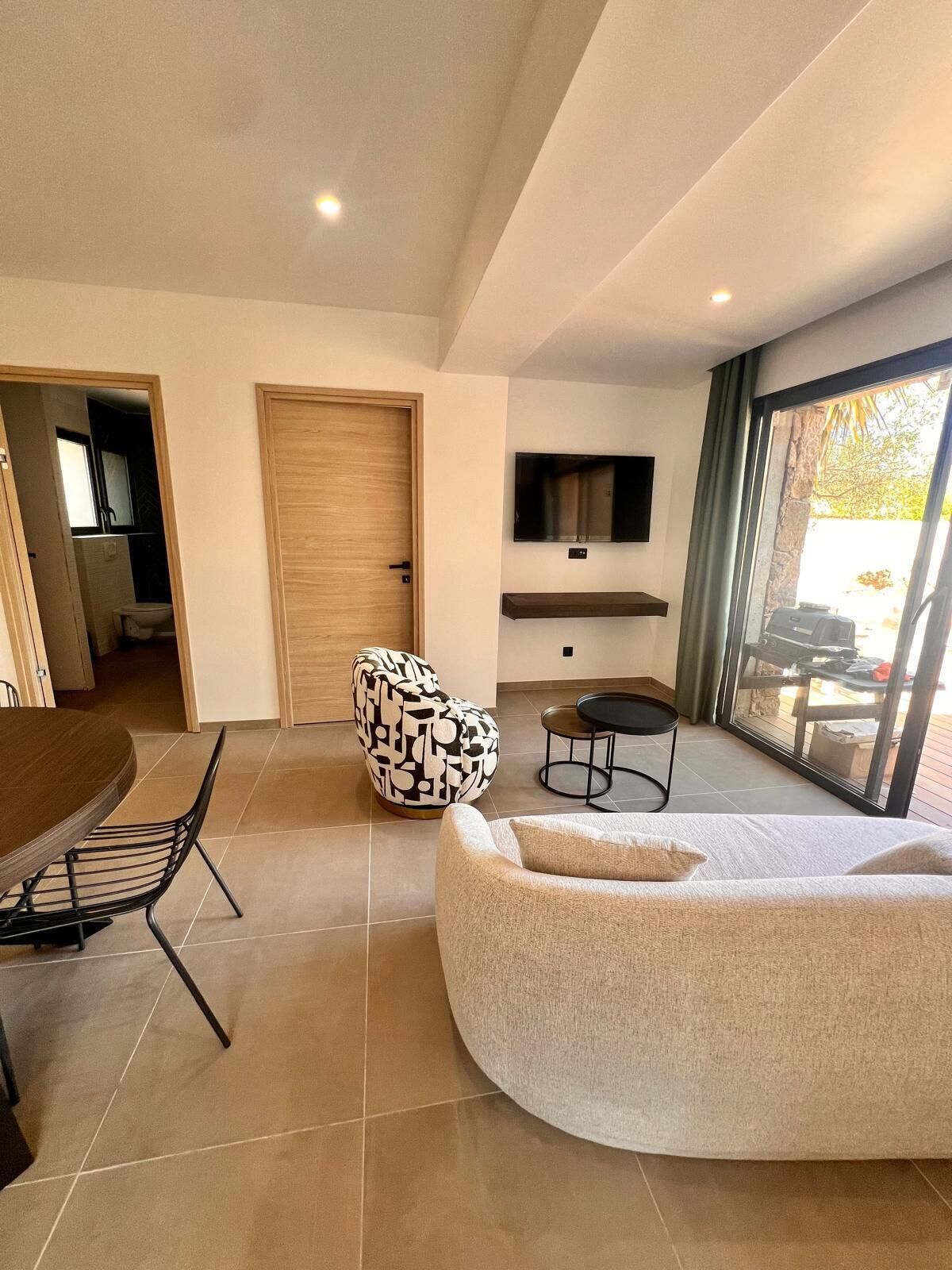 Un salon moderne comprenant un coin repas, une grande fenêtre et un téléviseur fixé au mur.