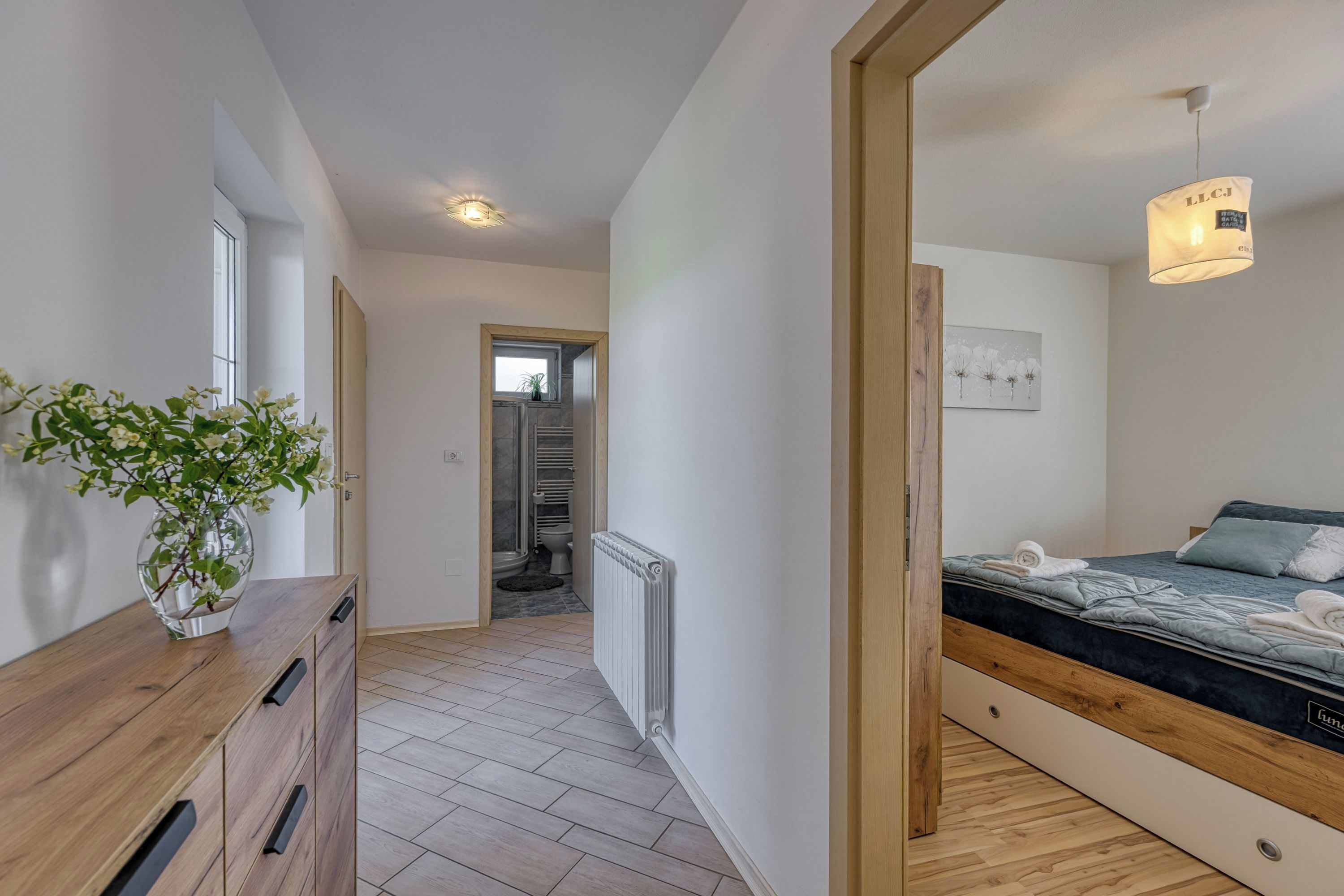 Un dormitorio con cama, cómoda de madera, radiador y un pasillo que da a un baño.