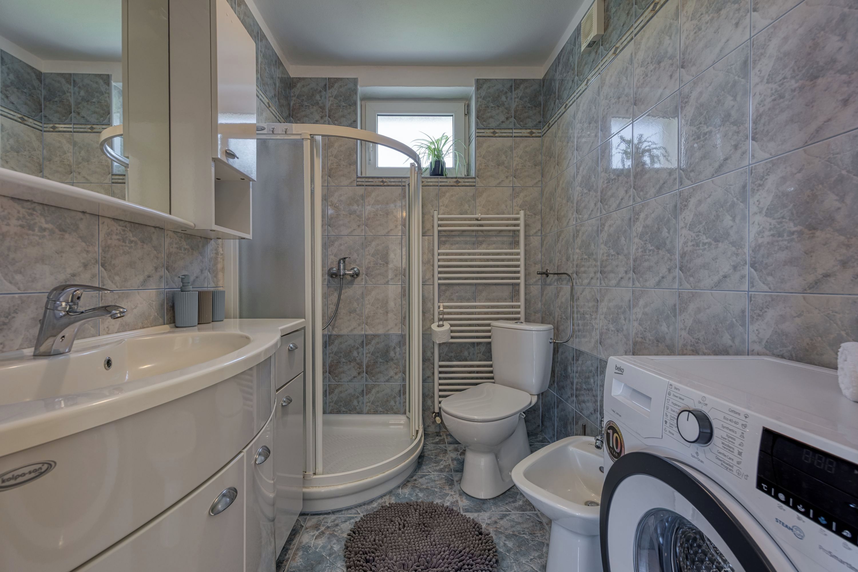 Une salle de bain moderne équipée d’une douche, de toilettes, d’un bidet et d’un lave-linge.