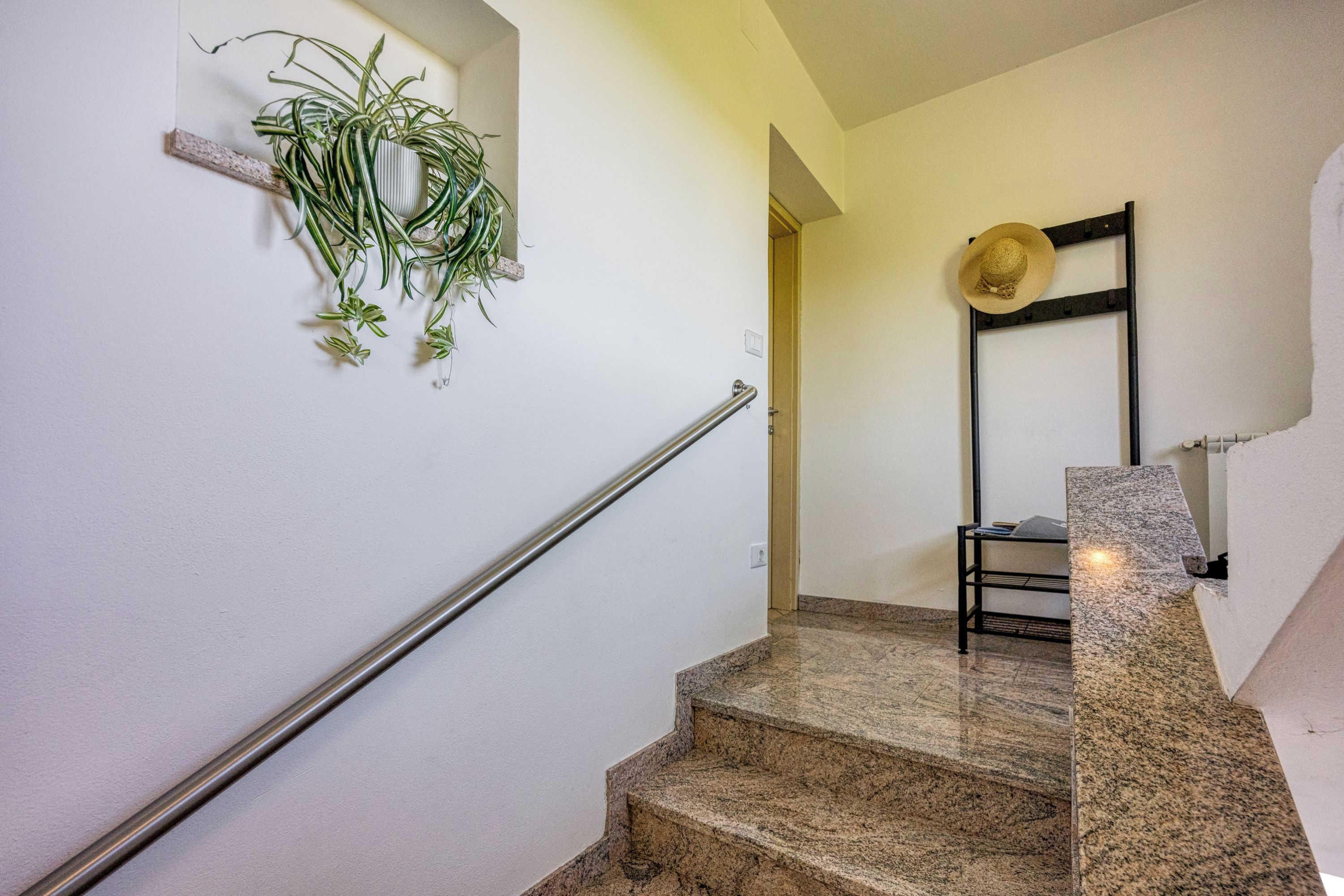 Una escalera con barandilla de metal, una planta en la pared y un sombrero en un perchero.