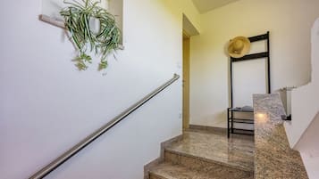 Una scala con corrimano in metallo, una pianta addossata al muro e un cappello su un appendiabiti.