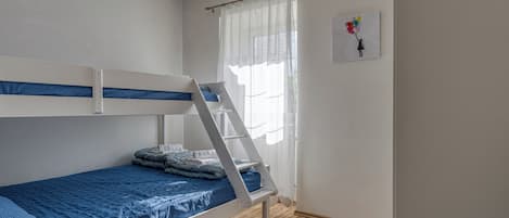 Habitación con literas, una escalera, una ventana con cortinas traslúcidas y una obra de arte en la pared.