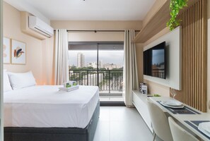 Une chambre d’hôtel moderne équipée d’un lit, d’une télévision, d’un bureau et d’un balcon offrant une vue sur la ville.