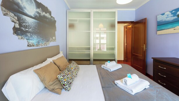 A hotel room with a bed, a nightstand, a dresser, and a large window.