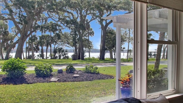 A view from a window overlooking a landscaped garden with trees and a body of water. - Riverside Rendezvous, Book Now Your Waterfront Vacation is calling! (Holly Hill)