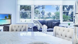 A modern living room with a large window, a television, a sofa, and a dining table. - Riverside Rendezvous, Book Now Your Waterfront Vacation is calling! (Holly Hill)
