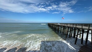 A wooden pier extending into the ocean with a flag at the end. - Riverside Rendezvous, Book Now Your Waterfront Vacation is calling! (Holly Hill)