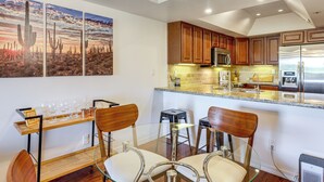 A modern kitchen with wooden cabinets, stainless steel appliances, and a glass dining table with chairs. - Golf Views & Pool Access: Central Scottsdale Condo (Scottsdale)