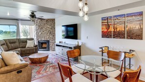 A modern living room with a stone fireplace, a flat-screen TV, and a dining area with a glass table and wooden chairs. - Golf Views & Pool Access: Central Scottsdale Condo (Scottsdale)