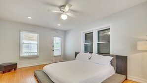 A bedroom with a bed, a ceiling fan, a door, and windows.