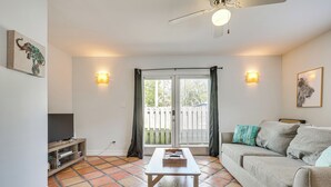 A living room with a sofa, a coffee table, a TV on a stand, and a sliding glass door leading to a balcony.