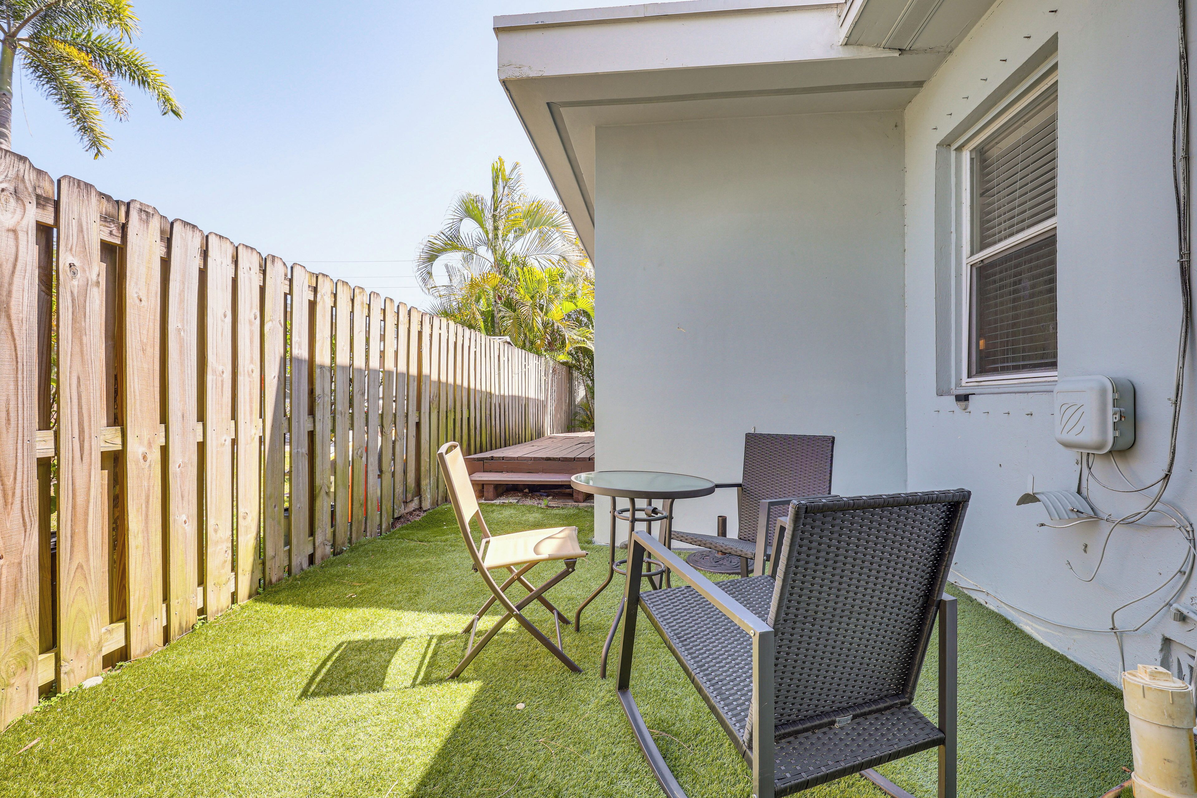 A patio with a wooden fence, a table, two chairs, and a small garden area.