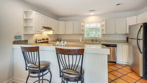 A kitchen with white cabinets, a stainless steel refrigerator, and a bar area with two stools.
