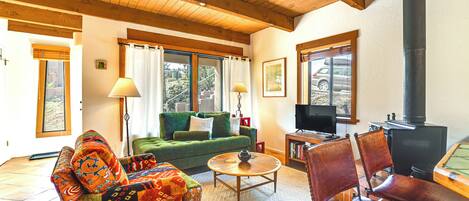 Una sala de estar acogedora con un sofá verde, un sillón estampado, una mesa de centro de madera y una chimenea.