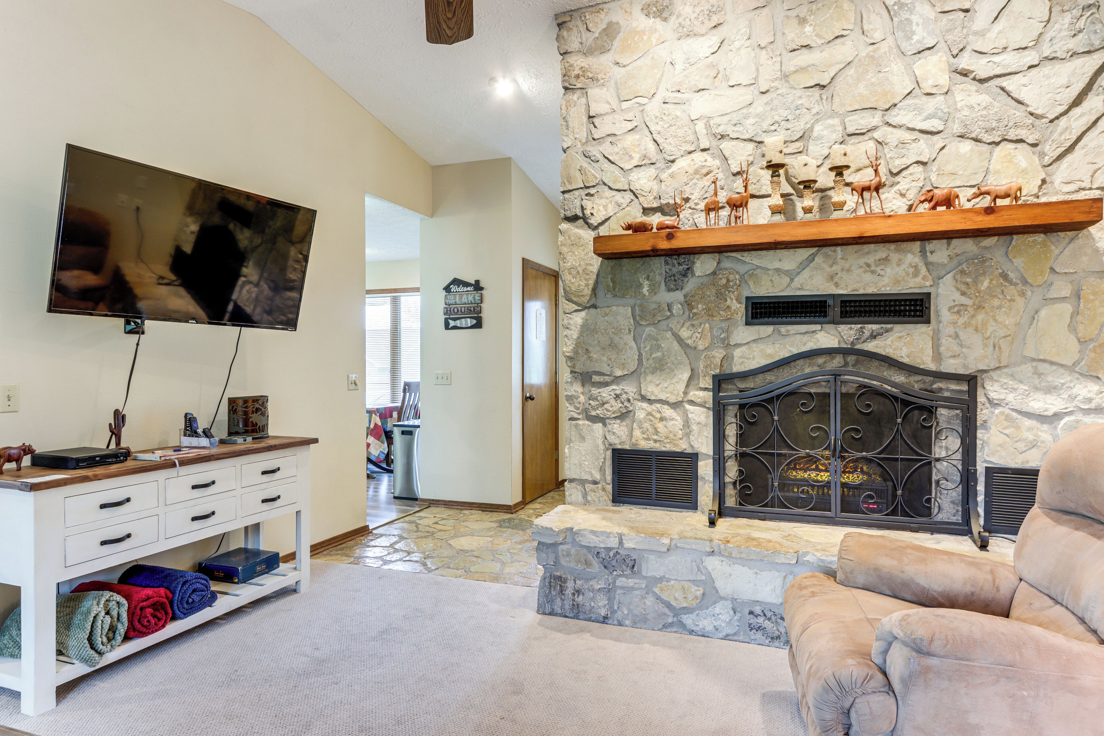 A living room with a stone fireplace, a mounted television, and a plush armchair.