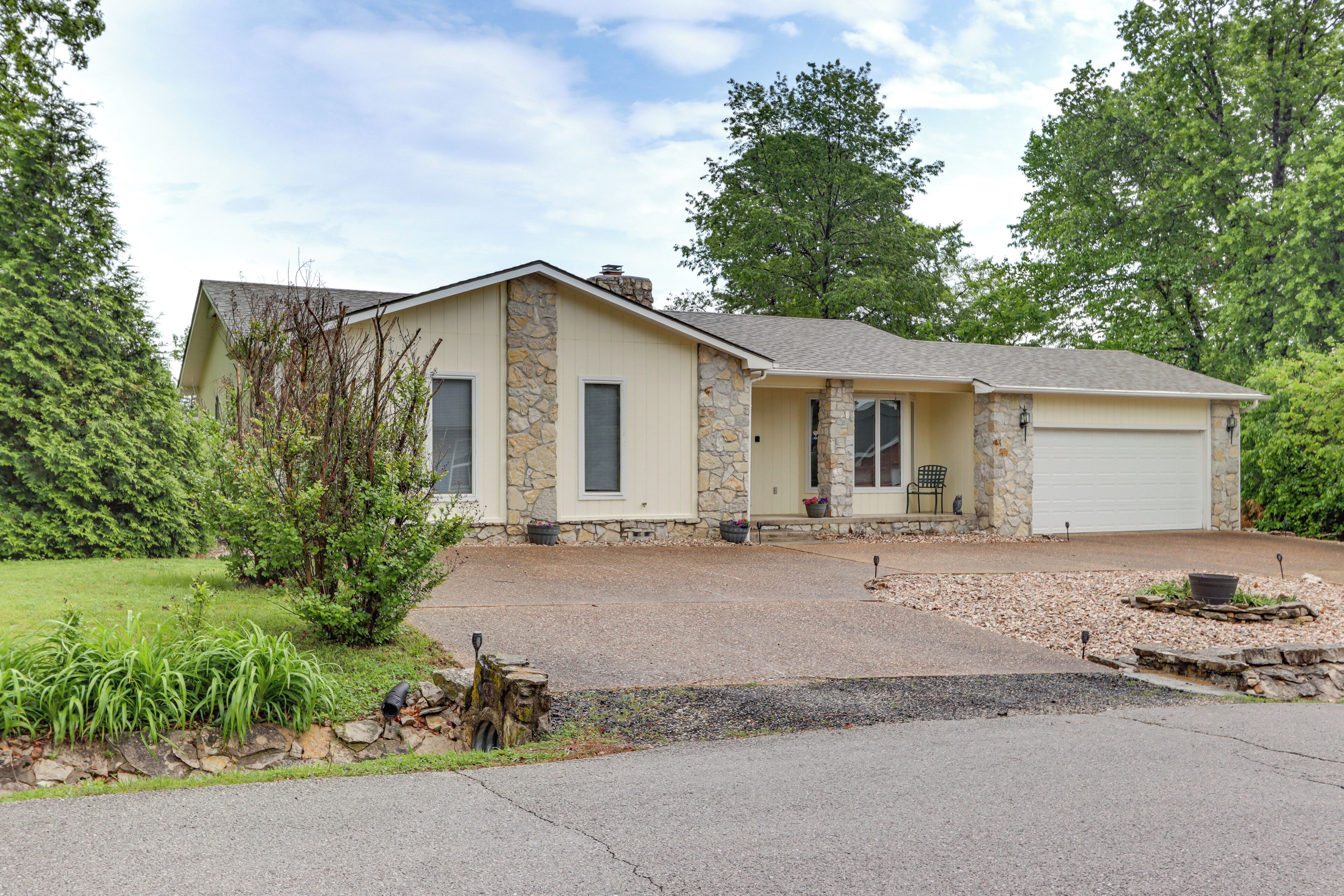 A two-story house with a stone facade, a garage, and a front yard with a small tree and shrubs.