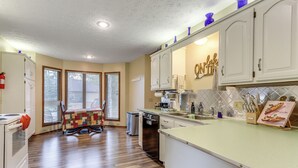 A kitchen with white cabinets, a dining table with a quilt, and a dishwasher. - Holiday Island Family Home on 13th Green! (Eureka Springs)
