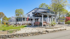 A two-story house with a covered porch, stone retaining wall, and a small garden area with outdoor seating.