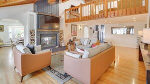 A spacious living area with a fireplace, wooden flooring, and a loft with a balcony.
