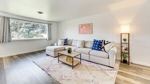 A modern living room with a sectional sofa, a coffee table, a patterned rug, a floor lamp, and a window with curtains. - Updated Family Home w/ Fenced Yard in Yakima! (Yakima)