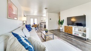 A modern living room with a sofa, coffee table, and TV stand. There is a dining area in the background with chairs and a table. - Updated Family Home w/ Fenced Yard in Yakima! (Yakima)