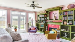 Una sala de estar con chimenea, estanterías verdes y un ventanal grande.