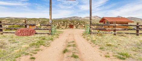 Un arco de madera con un letrero que dice "Spencer" y "Wildcat Ranch" que conduce a un edificio rústico con techo rojo.