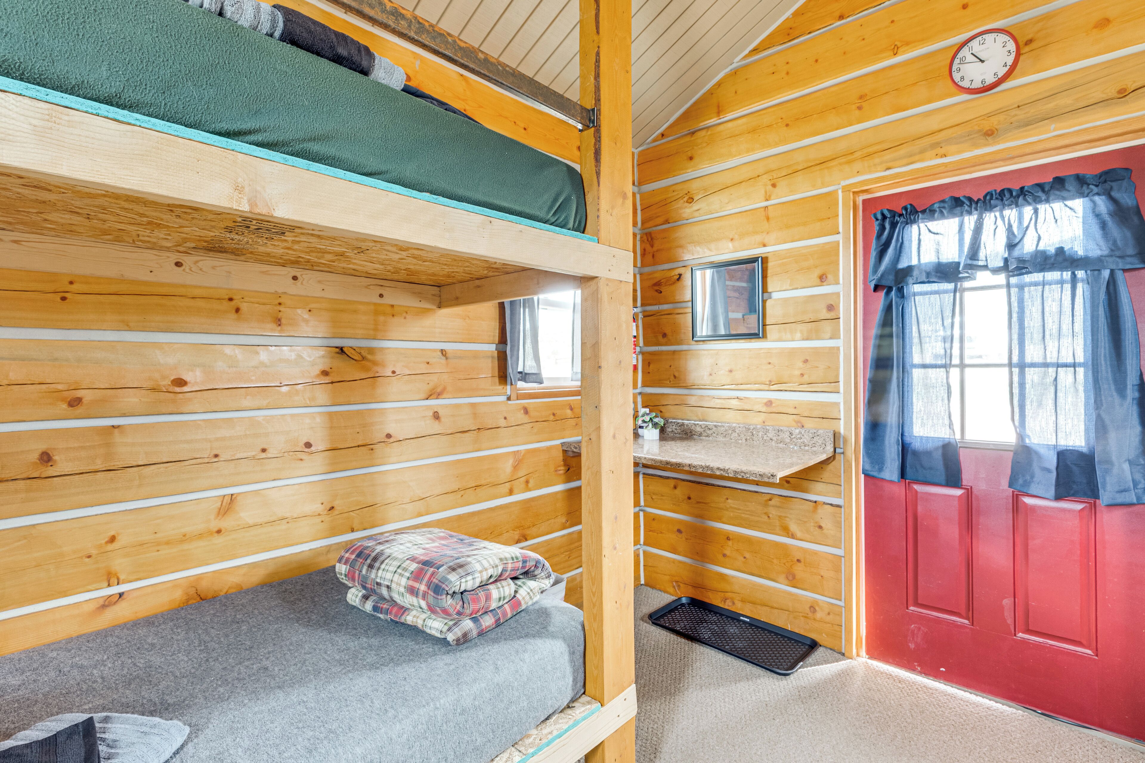 A wooden cabin with bunk beds, a red door, and a clock on the wall.