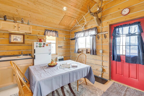 A wooden cabin interior with a dining table, chairs, a red door, and a refrigerator. - Sunset & Mtn Views: Rustic Colorado Retreat! (Maybell)