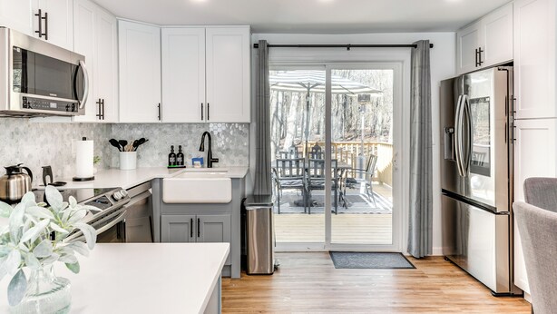 Una cocina moderna con armarios blancos, electrodomésticos de acero inoxidable y vistas a una terraza exterior.