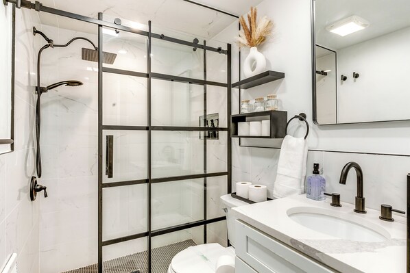 A modern bathroom with a glass-enclosed shower, a white sink with a mirror, and a toilet. - Poconos Hot Tub Haven! 14 Mi to Camelback Resort (Tobyhanna)