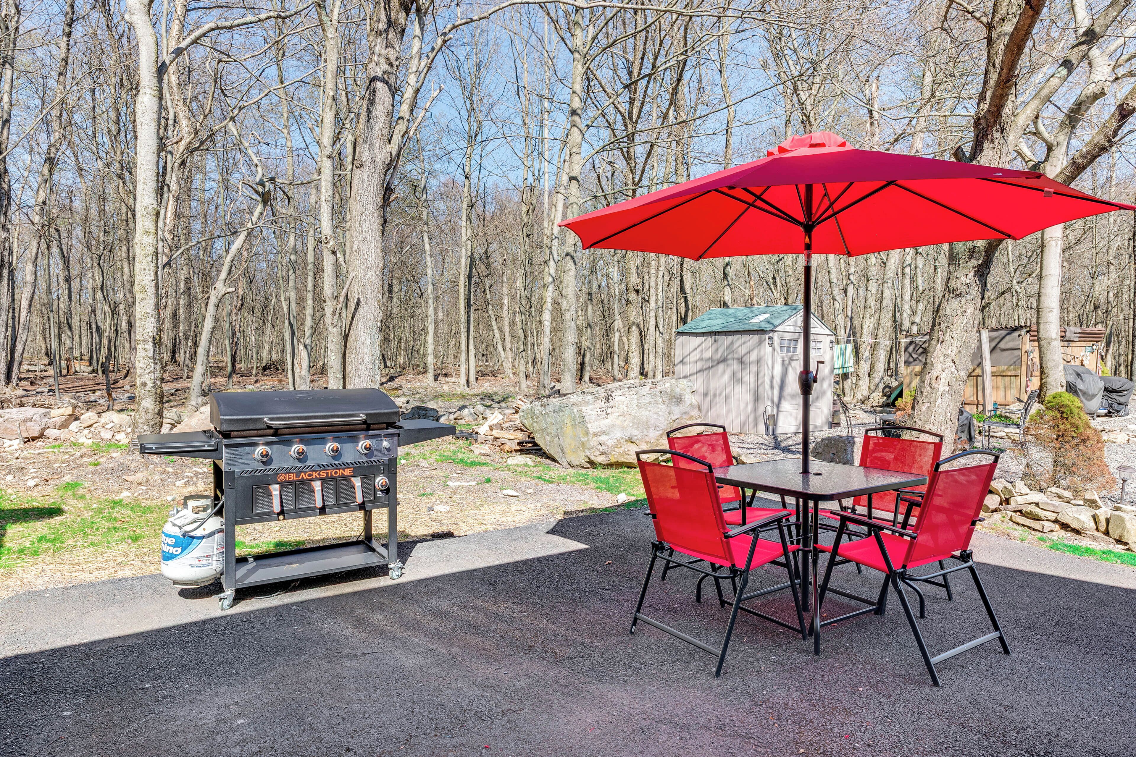 Un espace extérieur aménagé pour les repas, avec un barbecue, des chaises rouges et un parasol rouge.