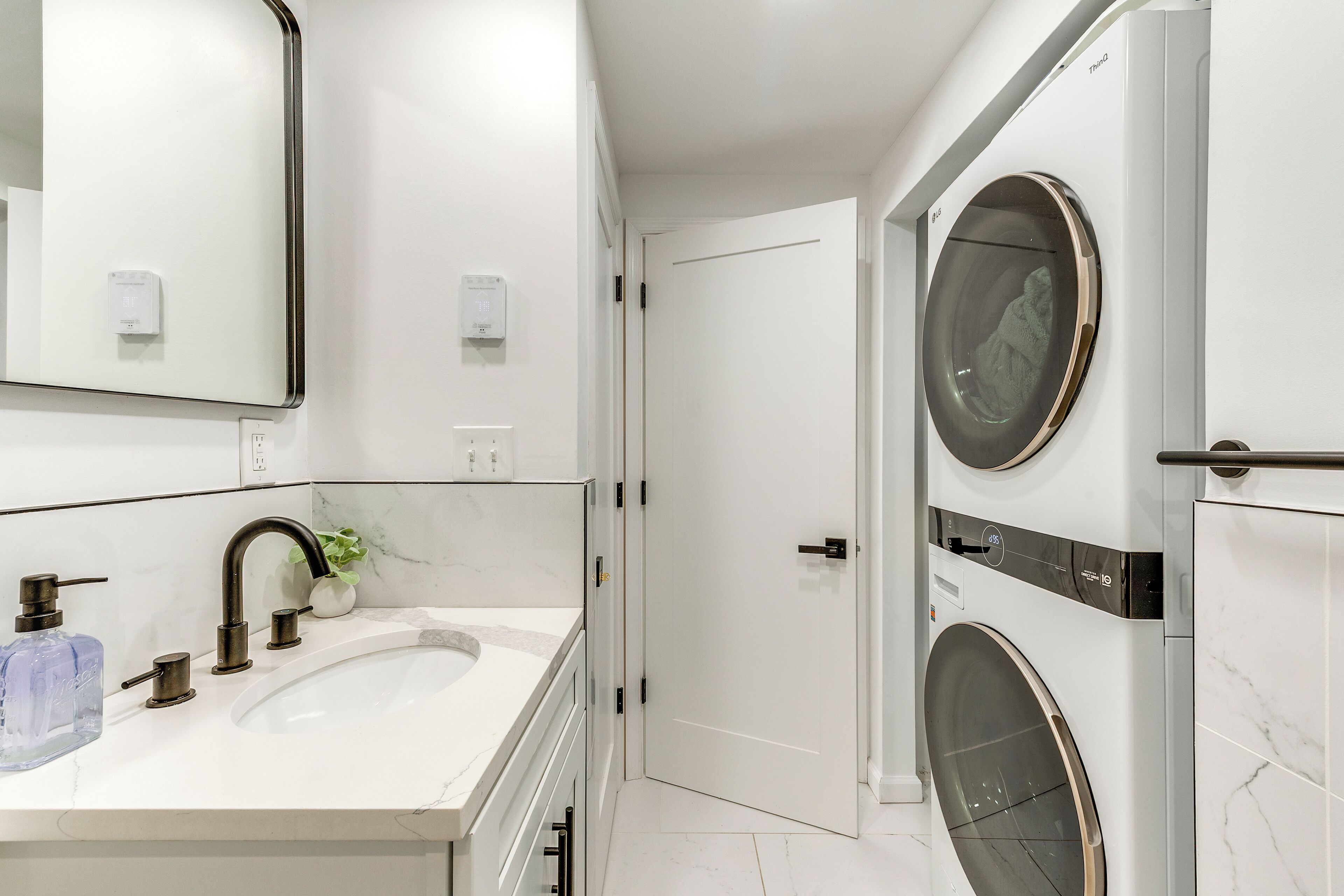 Une salle de bain moderne avec un lavabo blanc, un miroir et un lave-linge encastré.