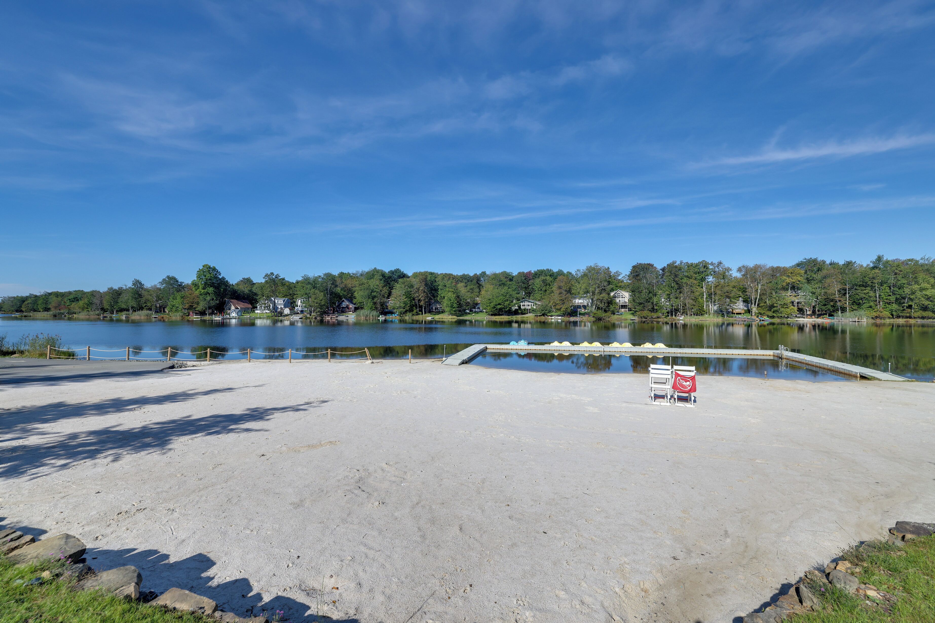 A lakeside area with a concrete dock, a small boat, and a row of houses in the background.