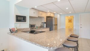A kitchen with granite countertops, stainless steel appliances, and a breakfast bar with stools. - Patio + Pond View: Serene Cape Cod Escape (Mashpee)